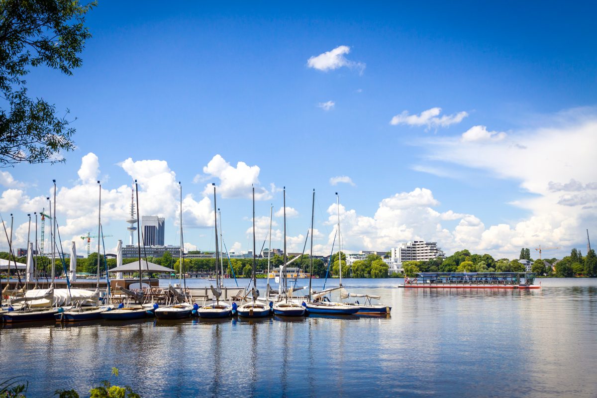 Segelboote auf der Alster in Hamburg in Deutschland. Im Hintergrund ist noch eine Fähre zu sehen, viel Wasser und blauer Himmel mit Wolken.